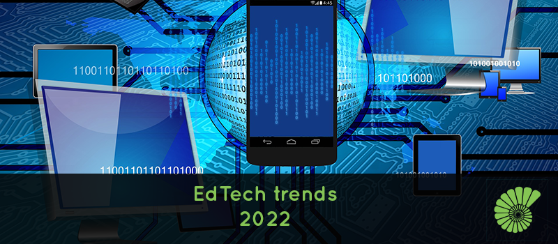 Different types of education devices, computers, tablets, phones surrounded by computer code language, text reads EdTech trends in 2022 with the Ammonite logo on the right hand side of the text